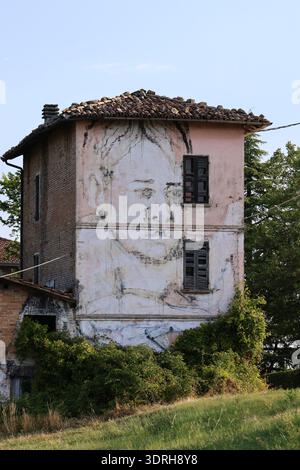 Large scale black and white portrait mural covering the facade of an abandoned rural building in Northern Italy featuring weathered brick walls and a Stock Photo