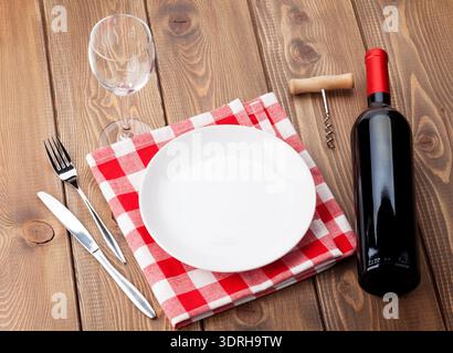 Table setting with empty plate, wine glass and red wine bottle Stock Photo
