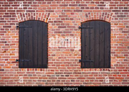 Two closed brown window shutters in a red brick facade Stock Photo