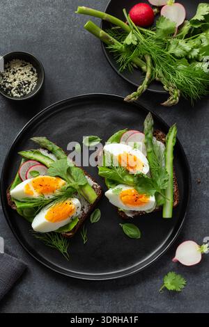 Sandwich with dark rye bread asparagus and soft boiled egg, healthy food, on black plate, top view Stock Photo