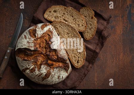 Sliced freshly baked homemade whole grain rye sour dough bread, top view, dark wooden background, copy space Stock Photo