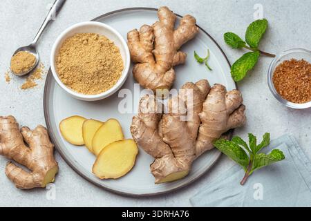 Sliced fresh ginger root,  ginger powder and mint leaves on plate, top view Stock Photo