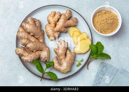 Sliced fresh ginger root,  ginger powder and mint leaves on plate, top view Stock Photo