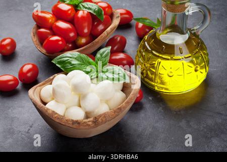 Mozzarella cheese, cherry tomatoes and basil herb leaves on stone table Stock Photo