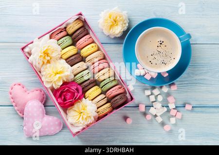 Colorful macaroons, coffee and marshmallow on wooden table. Sweet macarons in gift box and hearts. Top view Stock Photo