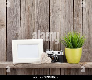 Blank photo frame, heart gift, camera and plant on shelf in front of wooden wall Stock Photo