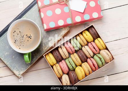 Colorful macaroons in a gift box and coffee cup on wooden table. Sweet macarons. Top view Stock Photo