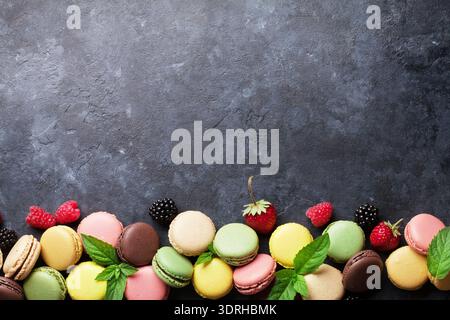 Colorful macaroons and berries on stone table. Sweet macarons with strawberry, raspberry and blackberry. Top view with copy spac Stock Photo