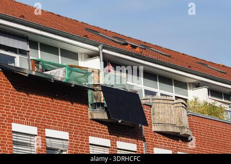 Several balconies are seen on a brick building. The balconies hold different plants and one has a solar panel. The rooftop shows some construction mat Stock Photo