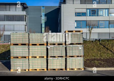 Pallets filled with bricks are stacked neatly next to a modern building on a sunny day. The blue sky highlights the structure in the background, creat Stock Photo