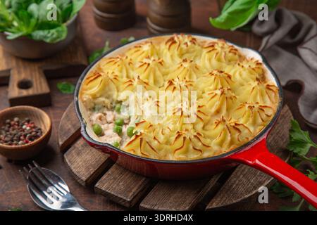 Salmon shepherds pie, salmon, vegetables and potato casserole, red cast iron pan, wooden background Stock Photo