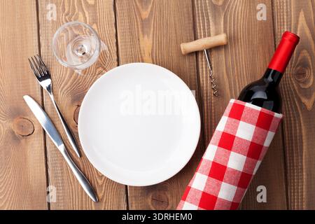 Table setting with empty plate, wine glass and red wine bottle Stock Photo