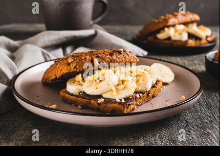 Sweet sandwich with chocolate butter, banana and nuts on a plate on the table Stock Photo