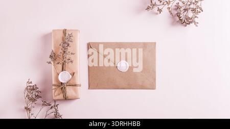 Gift in kraft paper and envelope with wax seals and dried flowers on pink top view web banner Stock Photo