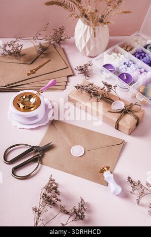 Craft envelope with wax seal and crafting items on pink vertical view Stock Photo