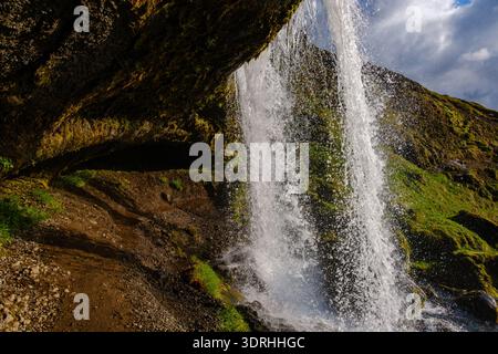 Majestic waterfall cascading over green cliffs in Iceland during bright daylight Stock Photo