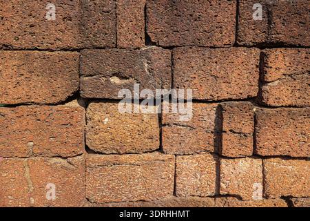 Weathered laterite stone wall with a porous reddish brown surface. Ancient masonry texture from a historical site in Thailand. Stock Photo