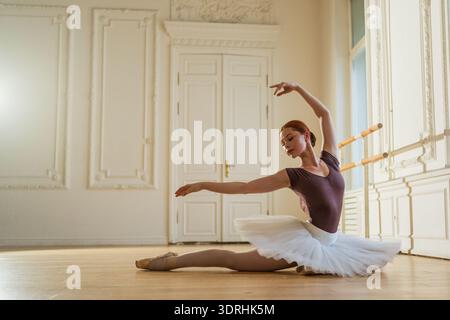 Young ballerina in tutu skirt stretching practicing ballet positions dancing in dance class. Young classical dancer woman in dan Stock Photo