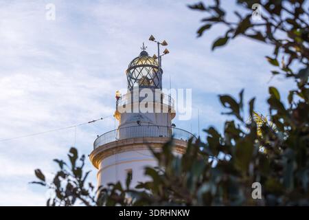 Malaga Spain close up view of the historic white lighthouse tower La Farola featuring the glass lantern room and antennas against a clear blue sky in Stock Photo