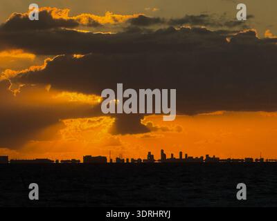 Golden clouds cast glow over city bay, serene ocean horizon captured during vibrant sunset moment Stock Photo