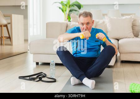 Fitness workout training. Senior man boxing punching picking up dumbbells. Old adult mature healthy man doing sports exercise at Stock Photo