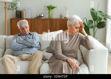 Marriage crisis relationship problems. Old couple quarreling. Sad mature disappointed woman sitting away from husband after havi Stock Photo