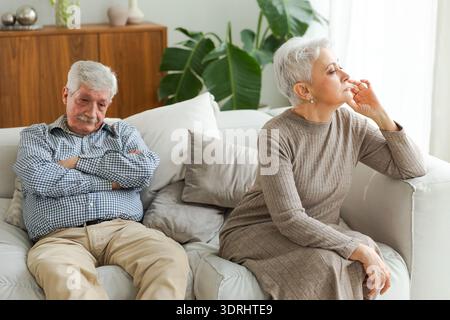 Marriage crisis relationship problems. Old couple quarreling. Sad mature disappointed woman sitting away from husband after havi Stock Photo