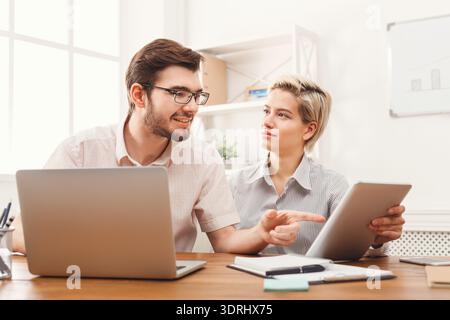 People Work Together on a Project Using Laptops and a Tablet in a Bright Office Setting Stock Photo