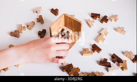 Female hand placing wooden puzzle piece into box on table Stock Photo