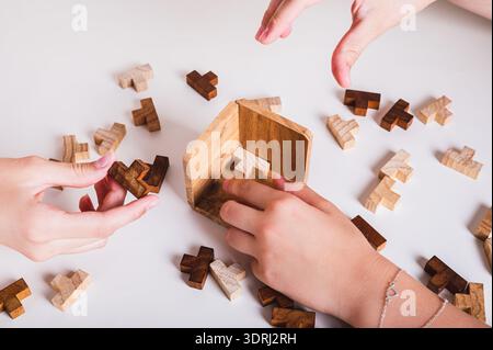 Children's hands assemble a puzzle of wooden figures on the table Stock Photo