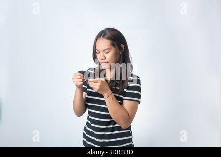 Indonesian woman in a striped shirt holding a smartphone with both hands, looking at the screen with focus. Isolated on white background. Stock Photo
