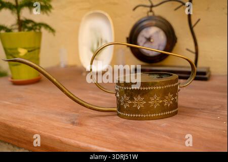 Vintage metal watering can on a wooden shelf with a clock and decorative plate. Concept of traditional gardening hobby, rustic interior accessories, a Stock Photo