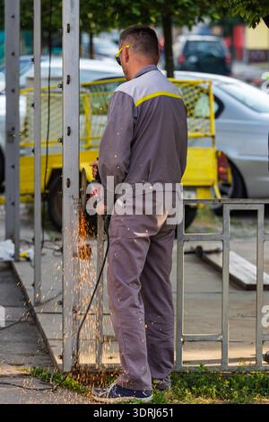 VINKOVCI, CROATIA, 05.19.2018:Construction worker wearing protective glasses grinds a metal post with an angle grinder, creating bright sparks while r Stock Photo