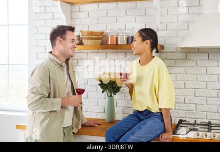 Happy couple relaxing with wine in cozy kitchen, smiling and talking together Stock Photo