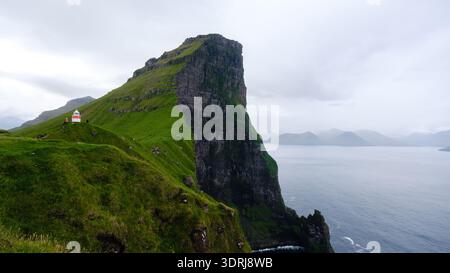 Breathtaking cliffs and lighthouse along the coast of the Faroe Islands under cloudy skies Stock Photo