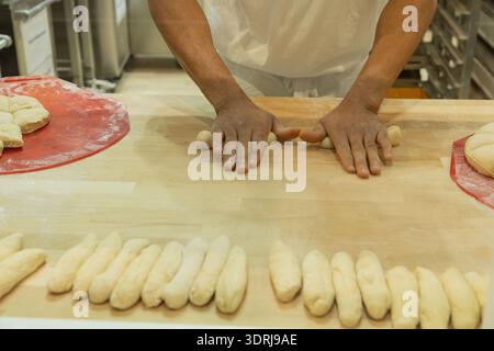 Baker shaping dough into rolls on a wooden countertop in a professional kitchen environment Stock Photo