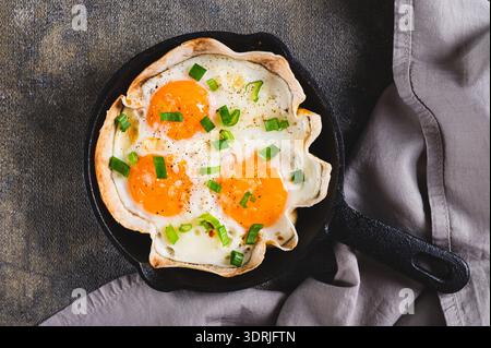 Close up of homemade scrambled eggs in pita bread with herbs in a frying pan on the table top view Stock Photo
