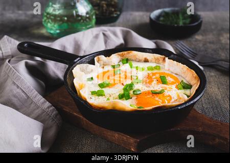Homemade scrambled eggs in pita bread with herbs in a frying pan on the table Stock Photo