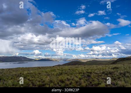 Lake Lagunillas in Peru is surrounded by rolling hills and grasslands, with dark storm clouds above and a distant rain shower fa Stock Photo
