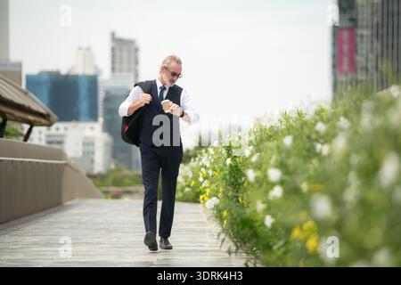 Senior businessman in a suit walking outdoors, checking the time on his watch Stock Photo