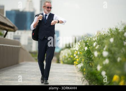 Senior businessman in a suit walking outdoors, checking the time on his watch Stock Photo