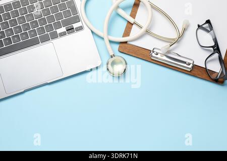 Stethoscope, clipboard, laptop and glasses on light blue background, flat lay. Space for text Stock Photo
