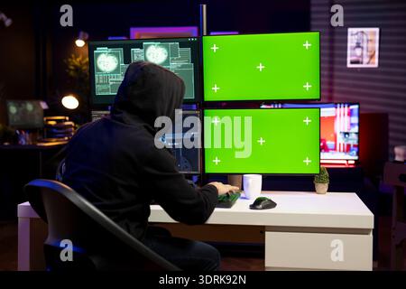 Hacker using malicious virus on green screen mockup PC to compromise devices and digital networks, gaining passwords. Man using chroma key isolated screen computer to steal and sell data online Stock Photo