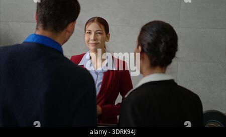 Happy couple checking in at hotel reception, smiling and talking Stock Photo