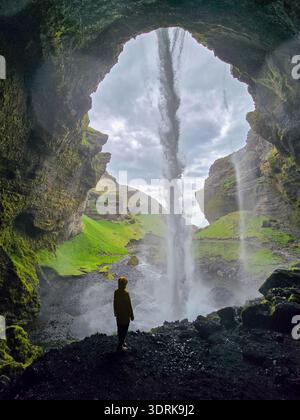 Majestic waterfall cascading through a cave with a silhouette in Iceland Stock Photo