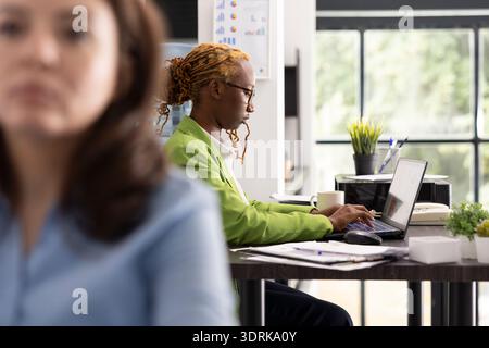 Professional female accountant reviewing company reports and financial data on laptop. Black woman consultant working at desk, analyzing business analytics and solving problems in corporate workplace. Stock Photo
