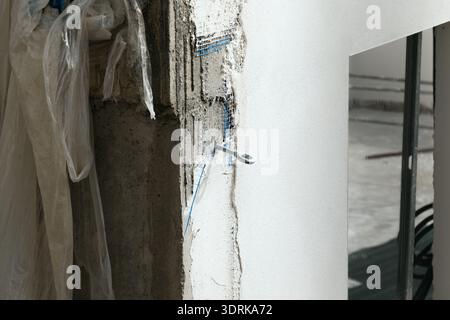 A close-up of a construction detail showing a metal hook set into a freshly plastered wall, with blue reinforcement mesh visible beneath the surface. Stock Photo