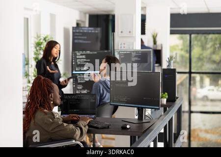 Black software developer in wheelchair studies frontend and backend code on computer screen. Focused professional demonstrates accessibility, problem solving and diversity within modern IT startup. Stock Photo
