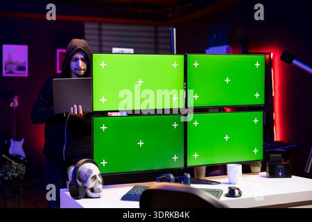 Hacker in office using laptop and exploits on isolated screen PC to break into systems and access restricted data. Man using mockup multi monitor setup VPN on dark web to sell sensitive information Stock Photo