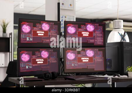 Desktop monitors show system error warnings in empty office workspace. The scene represents software failure, technical issues and business interruption in modern IT environment. Stock Photo